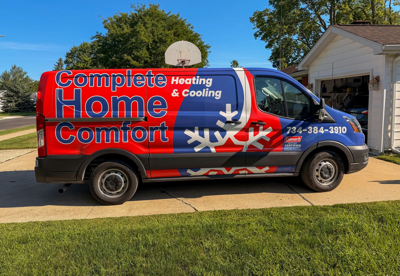 A red, white and blue Complete Home Comfort service van parked outside a home.